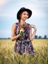 Cute attractive girl with a bouquet of colorful flowers in her hands. Young woman breathes in the scent of plants on wheat field