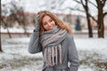Cute attractive pretty young woman in gray gloves in a trendy gray coat with a vintage knitted scarf is standing and smiling