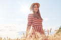 Cute attractive young girl with straw hat and striped stylish dress, posing on wheat field during sunset, enjoying beautiful Royalty Free Stock Photo