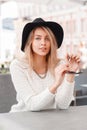 Cute attractive young woman in a white vintage knitted sweater in an elegant hat sitting on a warm spring day in an outdoor cafe. Royalty Free Stock Photo