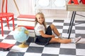 Cute ÃÂaucasian girl in a white blouse and black pleated skirt sitting in a school interior