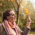 Cute autumn woman looking through yellow maple leaf outdoors. Romantic girl in fall park Royalty Free Stock Photo