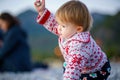 A cute baby in a beautiful sweater on the shore of the winter sea plays with stones. Beautiful child in nature.