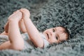 Cute baby with blue eyes lying on gray sheet in bedroom and holding her legs Royalty Free Stock Photo