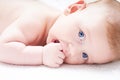 Cute baby with blue eyes sucks fingers, fist. On a light background Close up