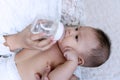 Cute baby boy drinking water from bottle with his mom. Hand of asian young woman holding bottle with water while feeding Royalty Free Stock Photo
