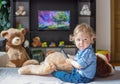 Cute baby boy and his dog plush toy watching TV sitting on a couch in the living room at home Royalty Free Stock Photo