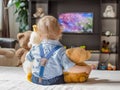 Cute baby boy and his teddy bear watching TV sitting on a couch in the living room at home Royalty Free Stock Photo