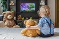 Cute baby boy and his teddy bear watching TV sitting on a couch in the living room at home Royalty Free Stock Photo