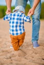 Cute baby boy learns to walk holding daddy`s hands on the beach on the sand Royalty Free Stock Photo