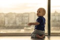 Cute baby boy looking through the window to the rainy big city. Infant boy waiting for the parents. Toddler kid sitting Royalty Free Stock Photo