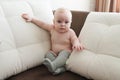 Cute baby 9 months old sits on a sofa in gray socks.