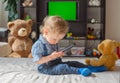 Cute baby boy playing with the remote control to watch TV sitting on a couch with his teddy bear, at home Royalty Free Stock Photo