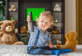 Cute baby boy playing with the remote control to watch TV sitting on a couch with his teddy bear, at home Royalty Free Stock Photo