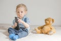 Cute baby boy playing with the remote control to watch TV sitting on a couch with his teddy bear, at home Royalty Free Stock Photo