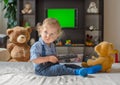 Cute baby boy playing with the remote control to watch TV sitting on a couch with his teddy bear, at home Royalty Free Stock Photo