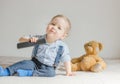 Cute baby boy playing with the remote control to watch TV sitting on a couch with his teddy bear, at home Royalty Free Stock Photo