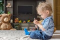 Cute baby boy playing with the remote control to watch TV sitting on a couch with his teddy bear, at home Royalty Free Stock Photo