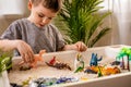 Cute baby boy playing sensory box kinetic sand table with carnivorous and herbivorous dinosaurs