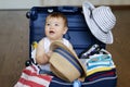 Cute baby boy sitting in the suitcase with hat in his hands, packed for vacation Royalty Free Stock Photo