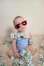 Cute baby boy in sunglasses playing with money, hundreds of dollars Royalty Free Stock Photo