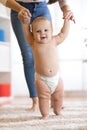 Cute baby boy taking first steps holding mother hands