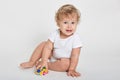 Cute baby boy toddler playing with toy car indoor, posing isolated over light background, wearing white bodysuit, looking directly Royalty Free Stock Photo