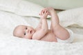 Cute baby lying on white sheet and holding his legs Royalty Free Stock Photo