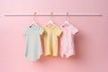 Cute baby clothes dresses hanging on hangers front view on colorful pastel pink background with copy space. Generative AI Royalty Free Stock Photo