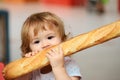 Cute baby eating French baguette white bread. Funny toddler child eating sandwich, self feeding concept. Royalty Free Stock Photo