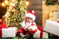 Cute baby face in Santa hat near Christmas tree. Happy Childhood, child 1 year old hold gift. New year kids. Royalty Free Stock Photo