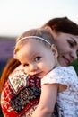 Cute baby girl with blonde curly hair wearing a white dress hugging her mom. Mother and baby daughter tender hugging Royalty Free Stock Photo