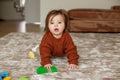 Cute baby girl crawling on floor at home, playing with colored building blocks. Brown sweater Royalty Free Stock Photo