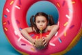 Cute baby girl drinking coconut water, posing with swim ring donought, blue color background. Tropical travel holidays. Royalty Free Stock Photo