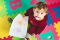 Cute baby girl with dummy on alphabet play mat drawing on paper with a colored crayon Royalty Free Stock Photo