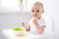 cute baby girl eating spaghetti pasta sitting in baby chair on white kitchen Royalty Free Stock Photo