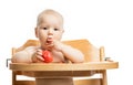 Cute baby girl eating tomato while sitting in high chair over white Royalty Free Stock Photo