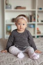 Cute baby girl with hairband ribbon on bed. Adorable child at home