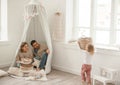 Cute baby girl with her parents play in a minimalistic children`s room.