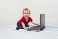 Cute baby girl holding laptop computer sitting on the bed, copy space Royalty Free Stock Photo