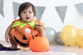 Cute baby girl kid dressing up in orange fancy Halloween pumpkin costume, cheerful little cute child holding orange pumpkin to Royalty Free Stock Photo