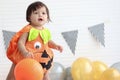 Cute baby girl kid dressing up in orange fancy Halloween pumpkin costume, cheerful little cute child holding orange pumpkin to Royalty Free Stock Photo