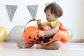 Cute baby girl kid dressing up in orange fancy Halloween pumpkin costume, cheerful little cute child holding orange pumpkin to Royalty Free Stock Photo