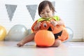 Cute baby girl kid dressing up in orange fancy Halloween pumpkin costume, cheerful little cute child holding orange pumpkin to Royalty Free Stock Photo