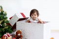 Cute baby girl kid in red costume holding ball ornament in gift present box near decorative Christmas tree, little child Royalty Free Stock Photo