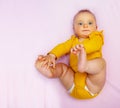Cute baby girl laying on the pink sheet hold legs