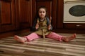 Cute baby girl, little baker confectioner in chef apron plays with wooden spoons, sitting barefoot on the kitchen floor