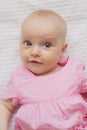 Cute baby girl in pink dress lies on white backgroun. Close-up portrait, cunning face.