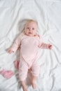 Cute baby girl in a pink suit smiling. Lying on a white sheet Royalty Free Stock Photo