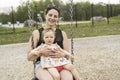 Cute baby girl playing on outdoor playground with mother on swing Royalty Free Stock Photo